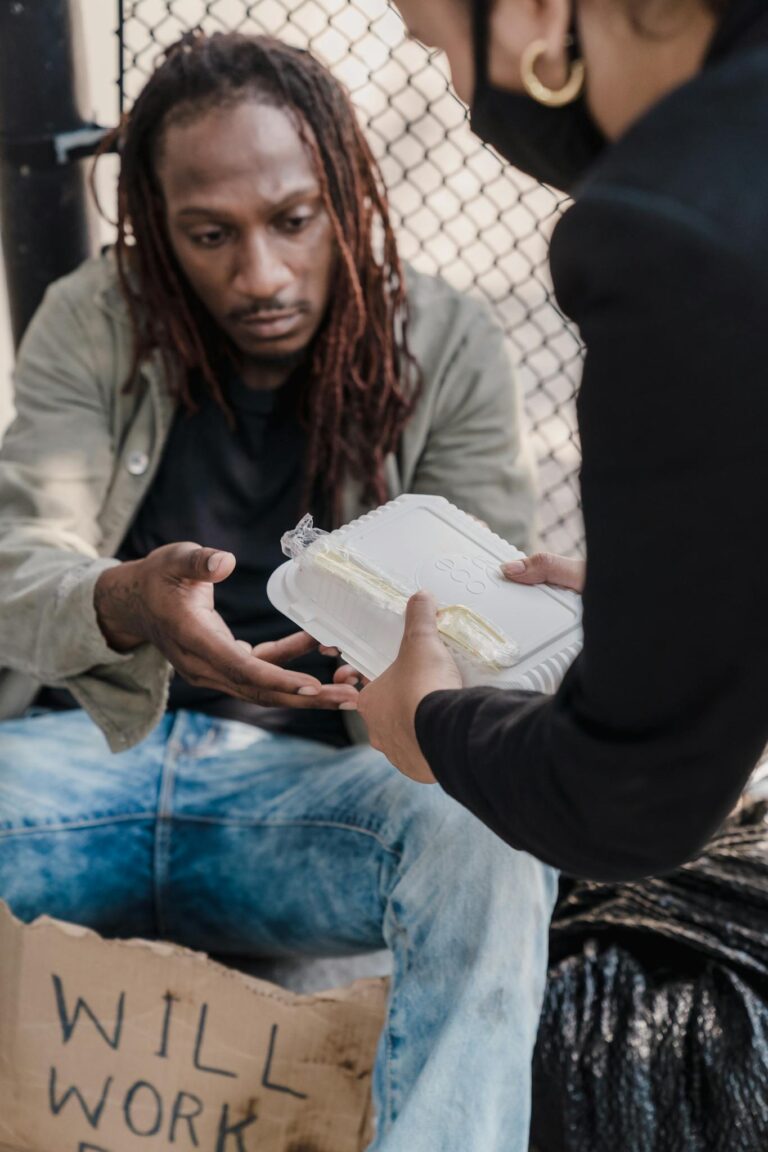 A person with dreadlocks receiving a meal from a helping hand on the street, showcasing kindness.